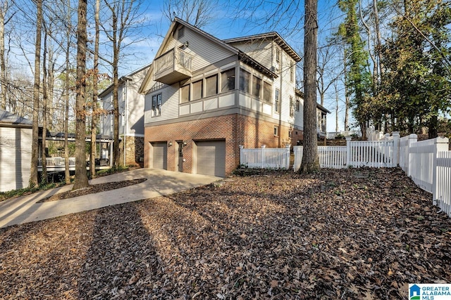 view of side of home featuring an attached garage, a balcony, brick siding, fence, and driveway