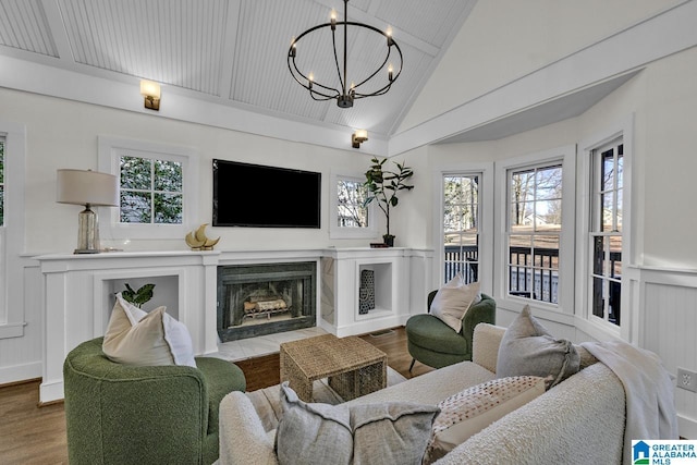 living room with a fireplace, wainscoting, vaulted ceiling, wood finished floors, and a chandelier