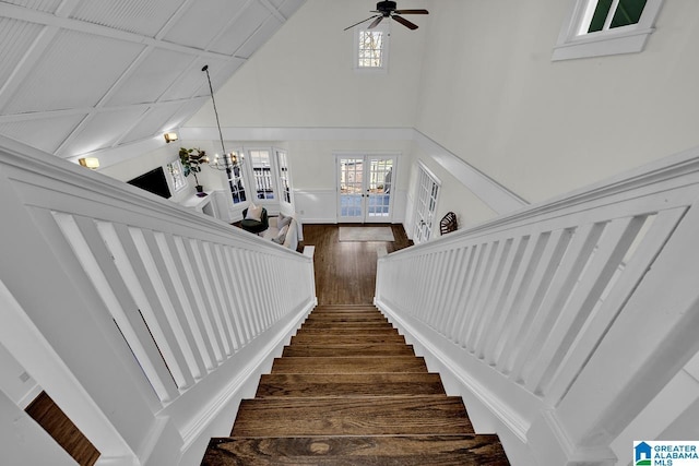 staircase with ceiling fan with notable chandelier, high vaulted ceiling, wood finished floors, and french doors