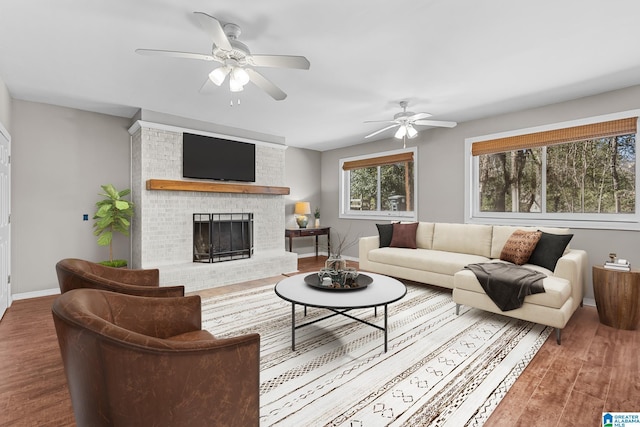 living room featuring ceiling fan, a brick fireplace, wood finished floors, and baseboards