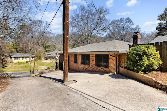 view of front facade with brick siding, a chimney, a shingled roof, fence, and driveway