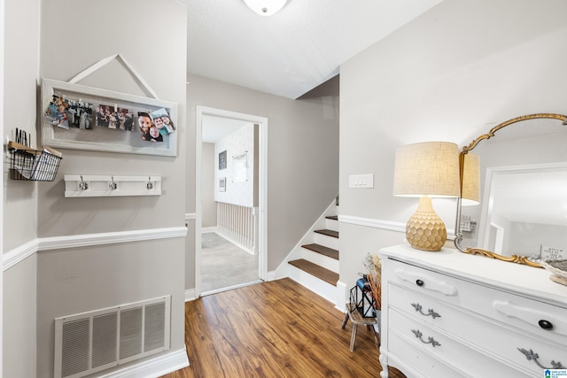 hallway featuring baseboards, visible vents, stairway, wood finished floors, and a textured ceiling