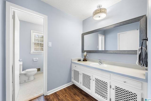 bathroom with a textured ceiling, toilet, wood finished floors, vanity, and baseboards