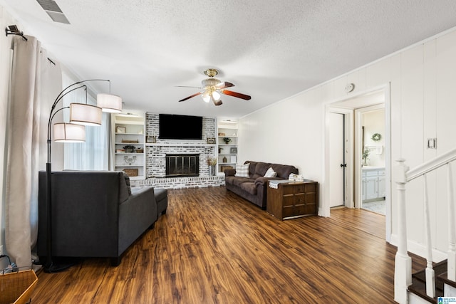 living area featuring a ceiling fan, dark wood-style floors, a textured ceiling, built in shelves, and a fireplace