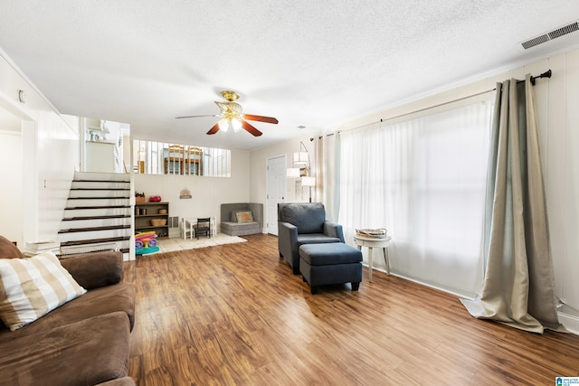 living room featuring a textured ceiling, wood finished floors, visible vents, a ceiling fan, and stairs