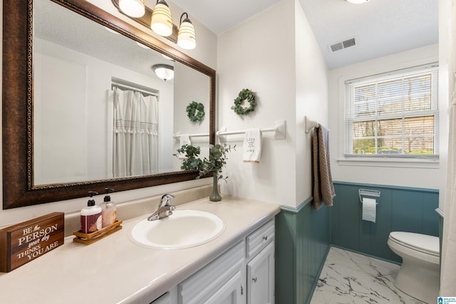 bathroom featuring visible vents, toilet, a wainscoted wall, marble finish floor, and vanity