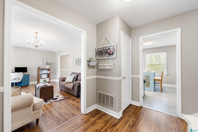 interior space featuring a notable chandelier, visible vents, a textured ceiling, wood finished floors, and baseboards