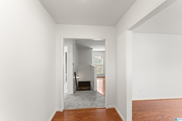 hall with a textured ceiling, wood finished floors, and baseboards