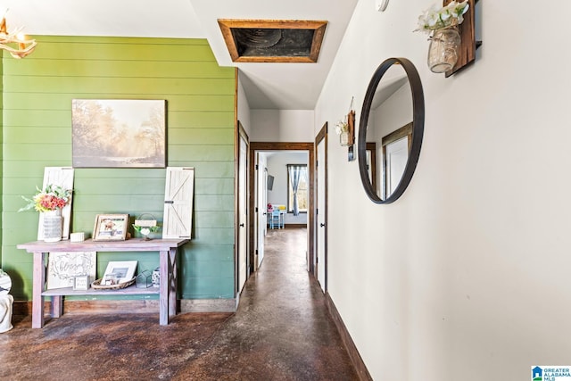 hall featuring wooden walls, baseboards, and concrete floors