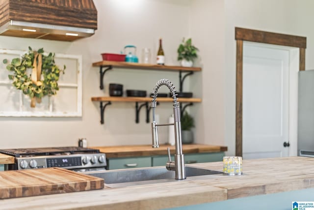 kitchen featuring open shelves, stainless steel gas stove, wooden counters, and a sink