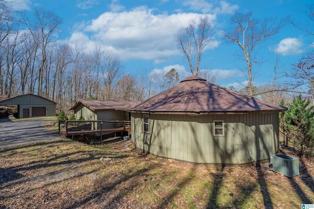 view of property exterior with a garage, central AC, an outdoor structure, and a wooden deck