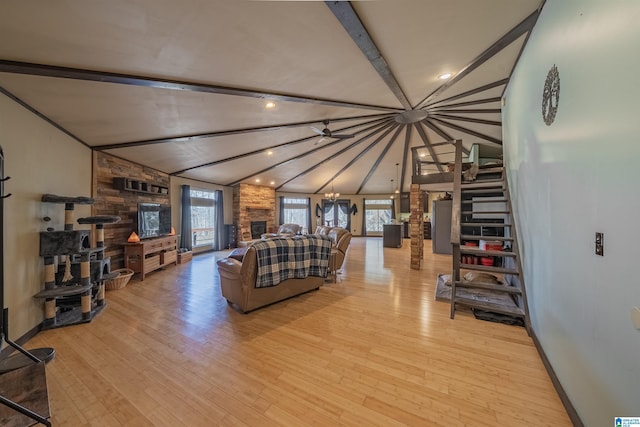 living area featuring baseboards, lofted ceiling with beams, a stone fireplace, light wood-type flooring, and a notable chandelier