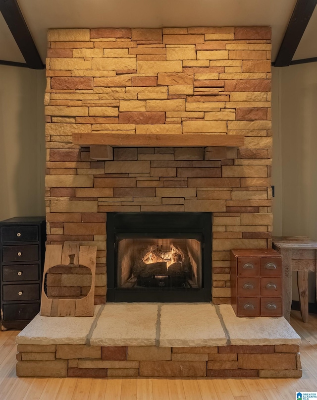 room details featuring beamed ceiling, a stone fireplace, and wood finished floors