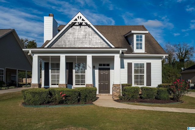 craftsman-style house with a shingled roof, a front yard, stone siding, and a chimney