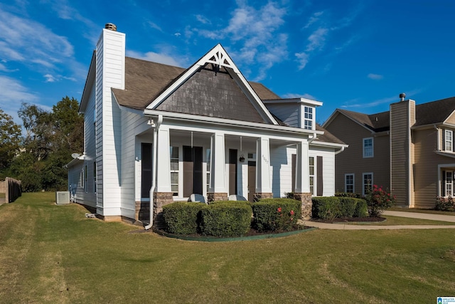 craftsman-style home featuring stone siding, central AC, a chimney, and a front lawn