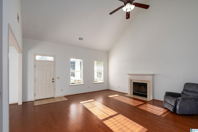 interior space with baseboards, visible vents, a fireplace with flush hearth, wood finished floors, and high vaulted ceiling