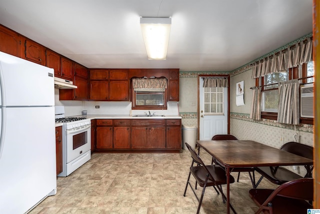 kitchen featuring light countertops, a sink, white appliances, under cabinet range hood, and wallpapered walls