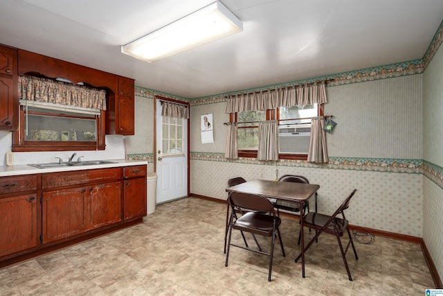 kitchen featuring wallpapered walls, baseboards, light countertops, light floors, and a sink