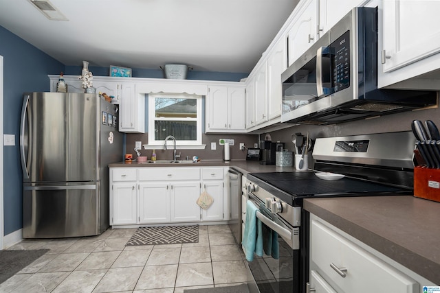 kitchen with light tile patterned floors, dark countertops, appliances with stainless steel finishes, white cabinetry, and a sink