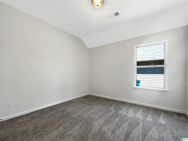 empty room featuring vaulted ceiling, dark colored carpet, visible vents, and baseboards