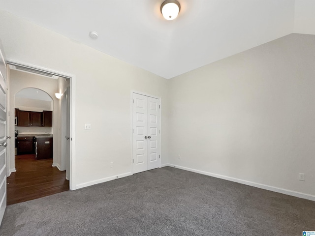 unfurnished bedroom with lofted ceiling, baseboards, dark carpet, and a closet