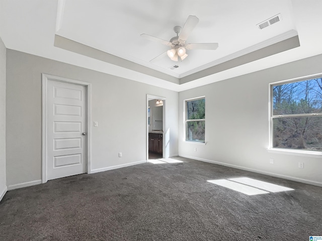 unfurnished bedroom with a tray ceiling, visible vents, dark colored carpet, and multiple windows