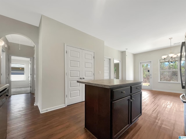 kitchen featuring arched walkways, a kitchen island, dark wood finished floors, and baseboards