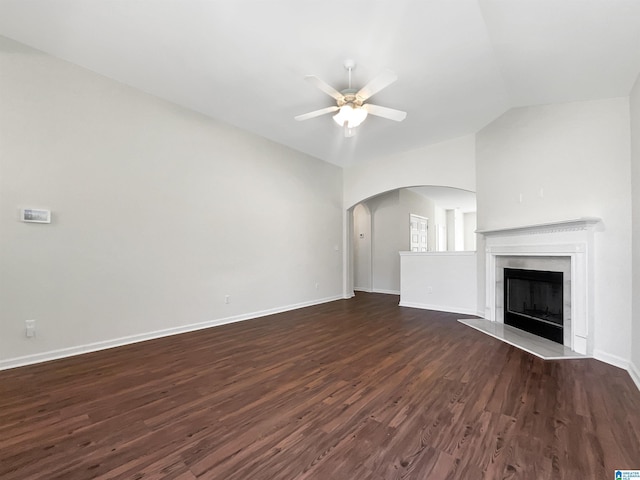 unfurnished living room featuring ceiling fan, a fireplace with raised hearth, arched walkways, vaulted ceiling, and dark wood finished floors