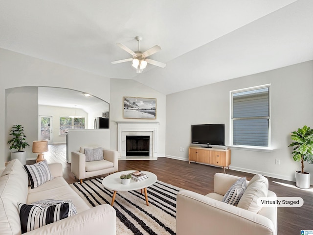 living room featuring lofted ceiling, a fireplace with raised hearth, a ceiling fan, wood finished floors, and baseboards