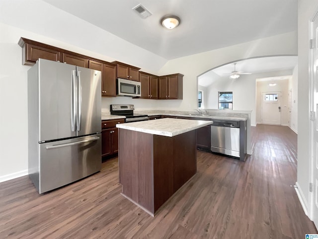 kitchen with arched walkways, lofted ceiling, a kitchen island, a peninsula, and stainless steel appliances