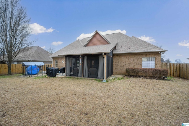 rear view of property featuring brick siding, roof with shingles, and a sunroom