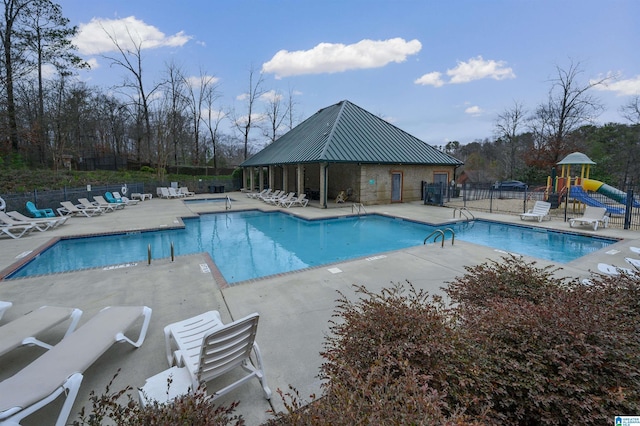 community pool featuring a patio area, playground community, and fence