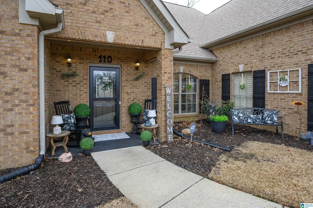 entrance to property featuring brick siding and roof with shingles