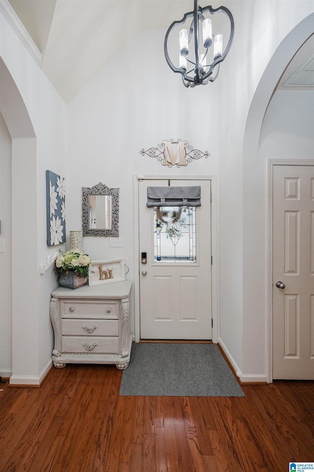 foyer entrance featuring arched walkways, dark wood-type flooring, a chandelier, and high vaulted ceiling