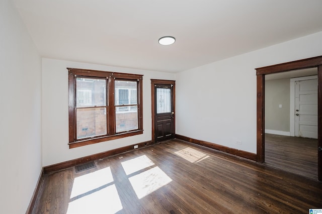 unfurnished room with baseboards, visible vents, and dark wood-style flooring