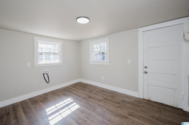 unfurnished room featuring dark wood-type flooring, plenty of natural light, and baseboards