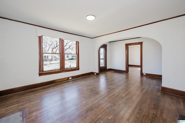 spare room featuring baseboards, arched walkways, wood finished floors, and ornamental molding