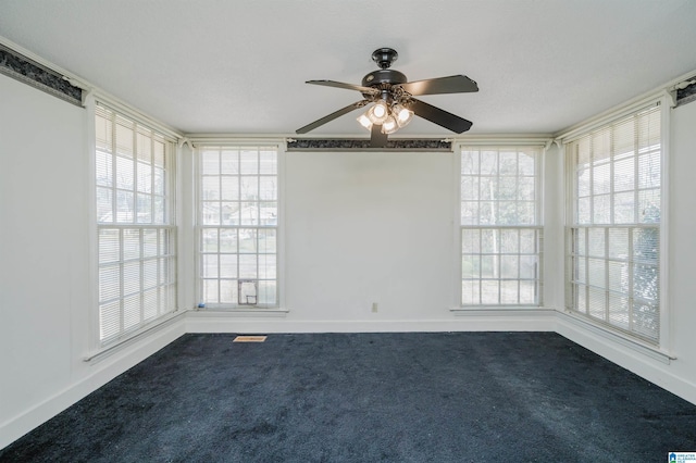 empty room with dark colored carpet, ceiling fan, and baseboards