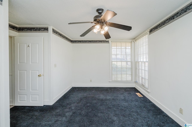 empty room with dark colored carpet, visible vents, crown molding, and baseboards