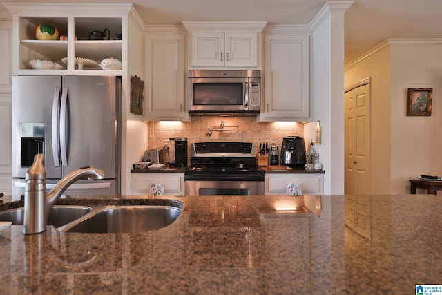 kitchen with white cabinets, dark stone counters, appliances with stainless steel finishes, a sink, and backsplash