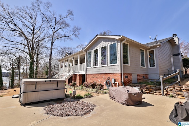 view of property exterior with a chimney, brick siding, a hot tub, and stairs