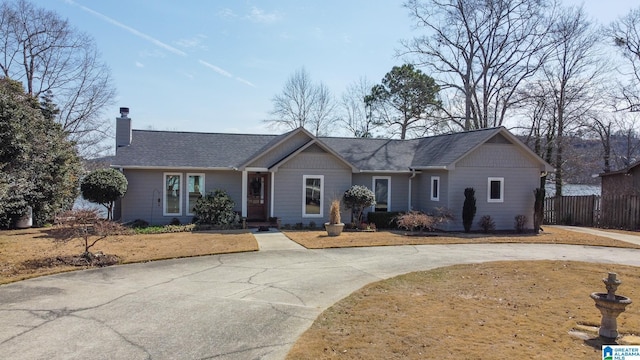 ranch-style house with a chimney, fence, and roof with shingles