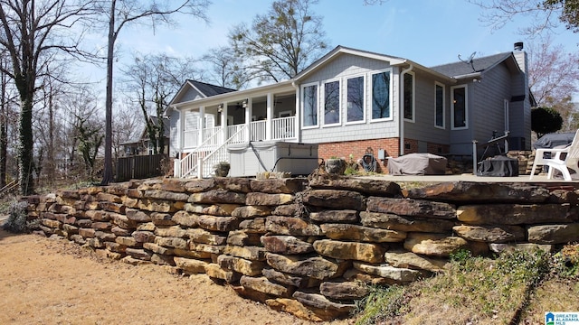 rear view of property featuring covered porch, brick siding, a chimney, and stairs