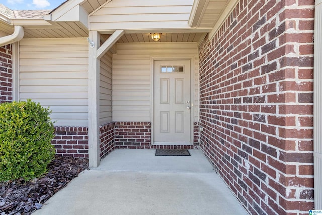 doorway to property with brick siding and a shingled roof