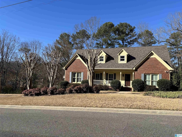 new england style home with brick siding, covered porch, and a shingled roof