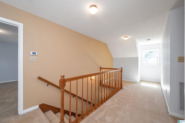 corridor featuring an upstairs landing, carpet flooring, and a textured ceiling