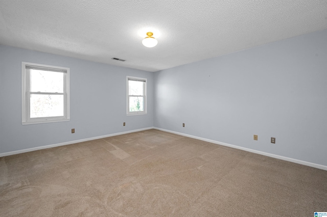 empty room featuring visible vents, baseboards, light colored carpet, and a textured ceiling