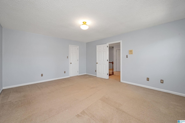 empty room featuring light colored carpet, a textured ceiling, and baseboards