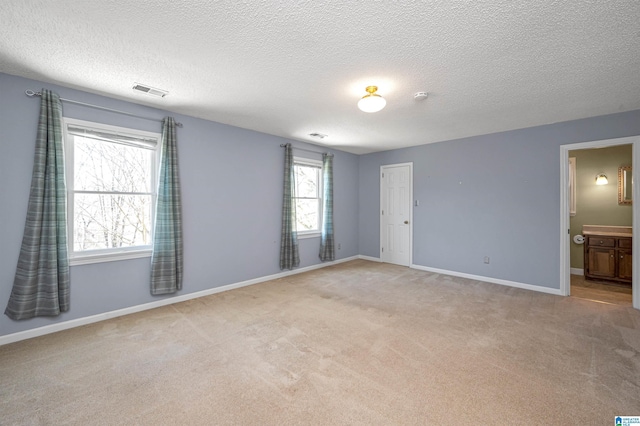 unfurnished bedroom with connected bathroom, baseboards, light colored carpet, and a textured ceiling