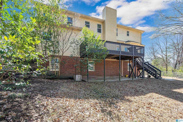 back of property with brick siding, a wooden deck, a chimney, and stairs